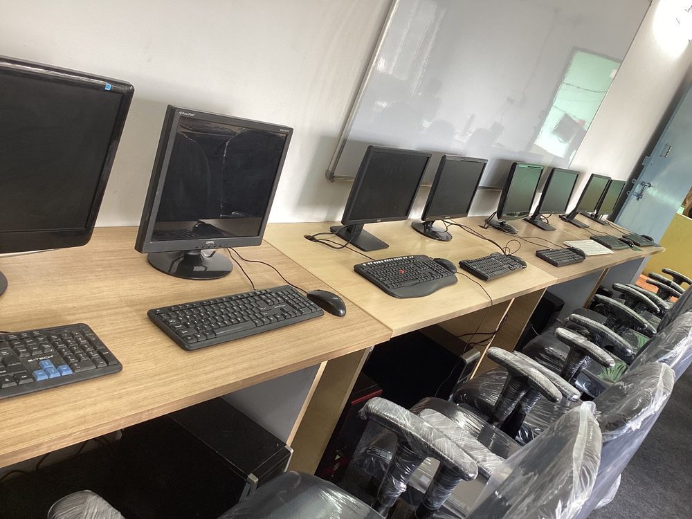A row of desktop computers along a wooden bench, with a whiteboard on the wall behind.