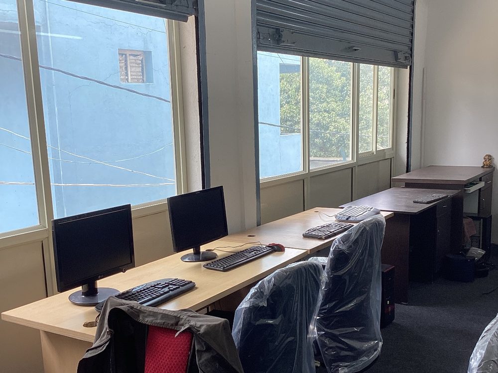 A second computer room with workstations along a bench under a bank of windows.